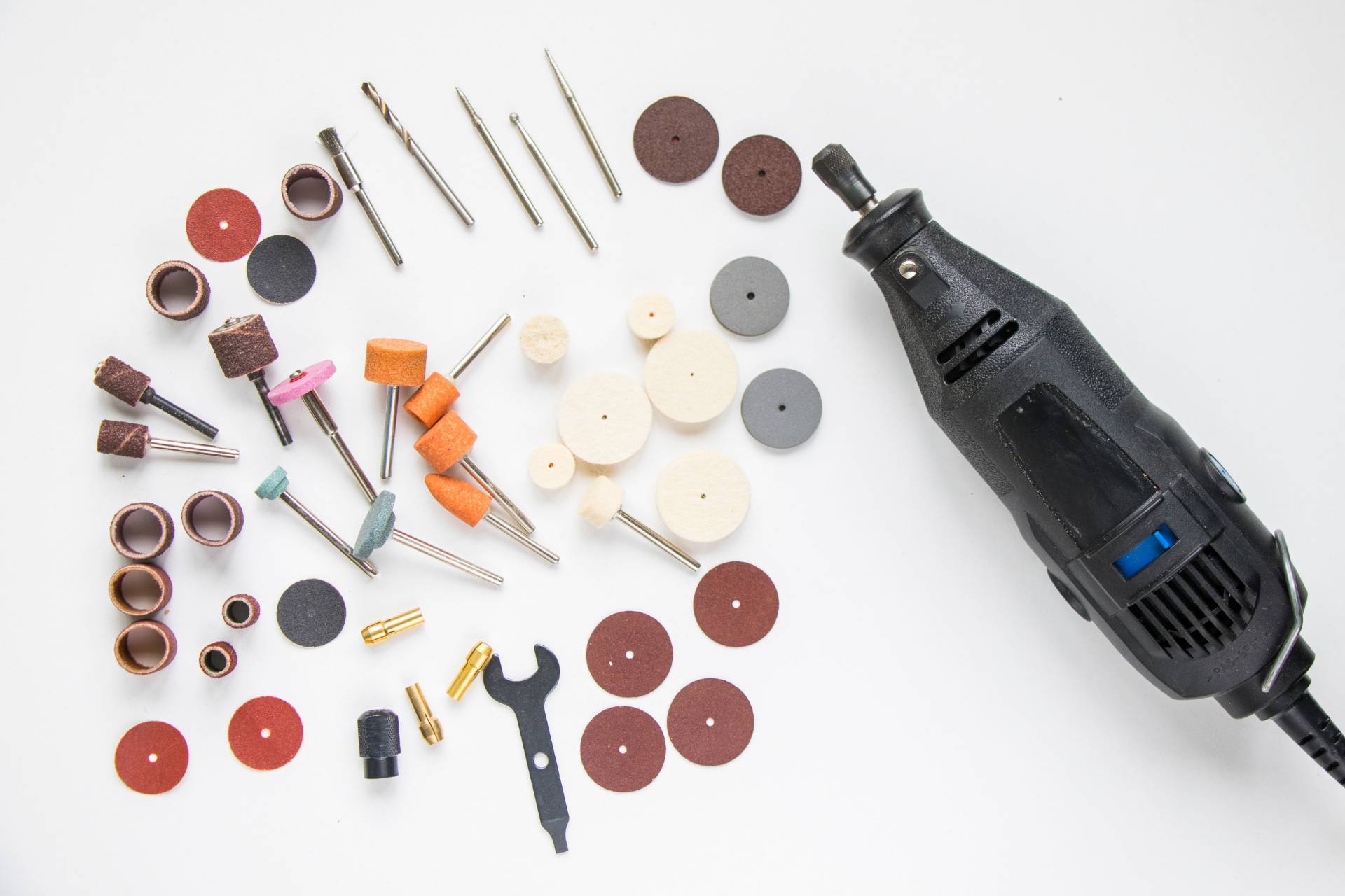 An array of rotary tool attachments including sanding discs, grinding bits, and polishing wheels laid out next to a rotary tool, showcasing the versatility of the tool for detailed work