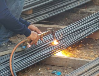 Worker using a blowtorch for precision cutting of rebar on a construction site.
