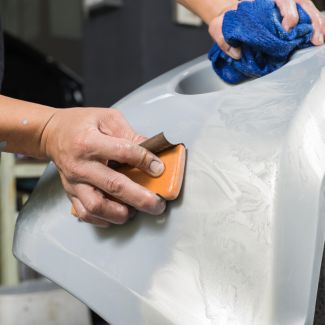 Auto body worker hand-sanding a car panel with sandpaper block for precise surface preparation