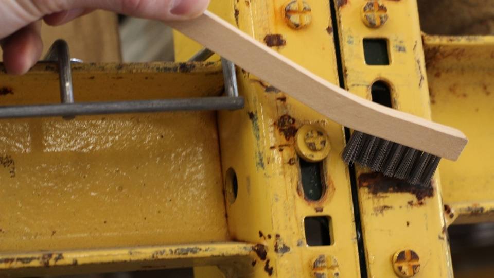 Using a handheld wire brush to remove rust from metal surfaces