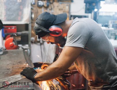 Worker in a workshop using a grinding tool with earmuffs for hearing protection, as recommended in Empire Abrasives guide to sanding and grinding PPE.