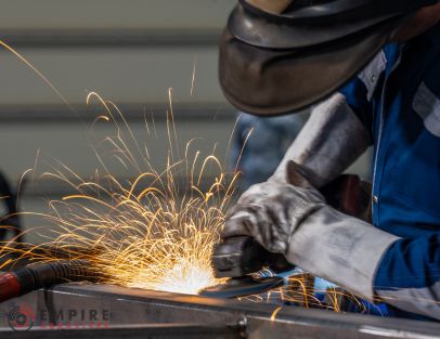 Metal worker wearing proper PPE including protective leather gloves for metal grinding with an angle grinder.