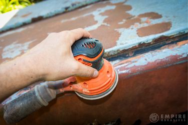 Palm sander being used for rust removal on car surface by a professional