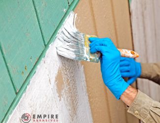Hand with blue glove applying white primer on wooden siding, demonstrating wood surface preparation for painting