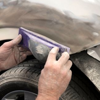 Auto body worker hand-sanding a car panel to achieve a smooth surface for primer application, highlighting the importance of surface preparation for paint adhesion and longevity