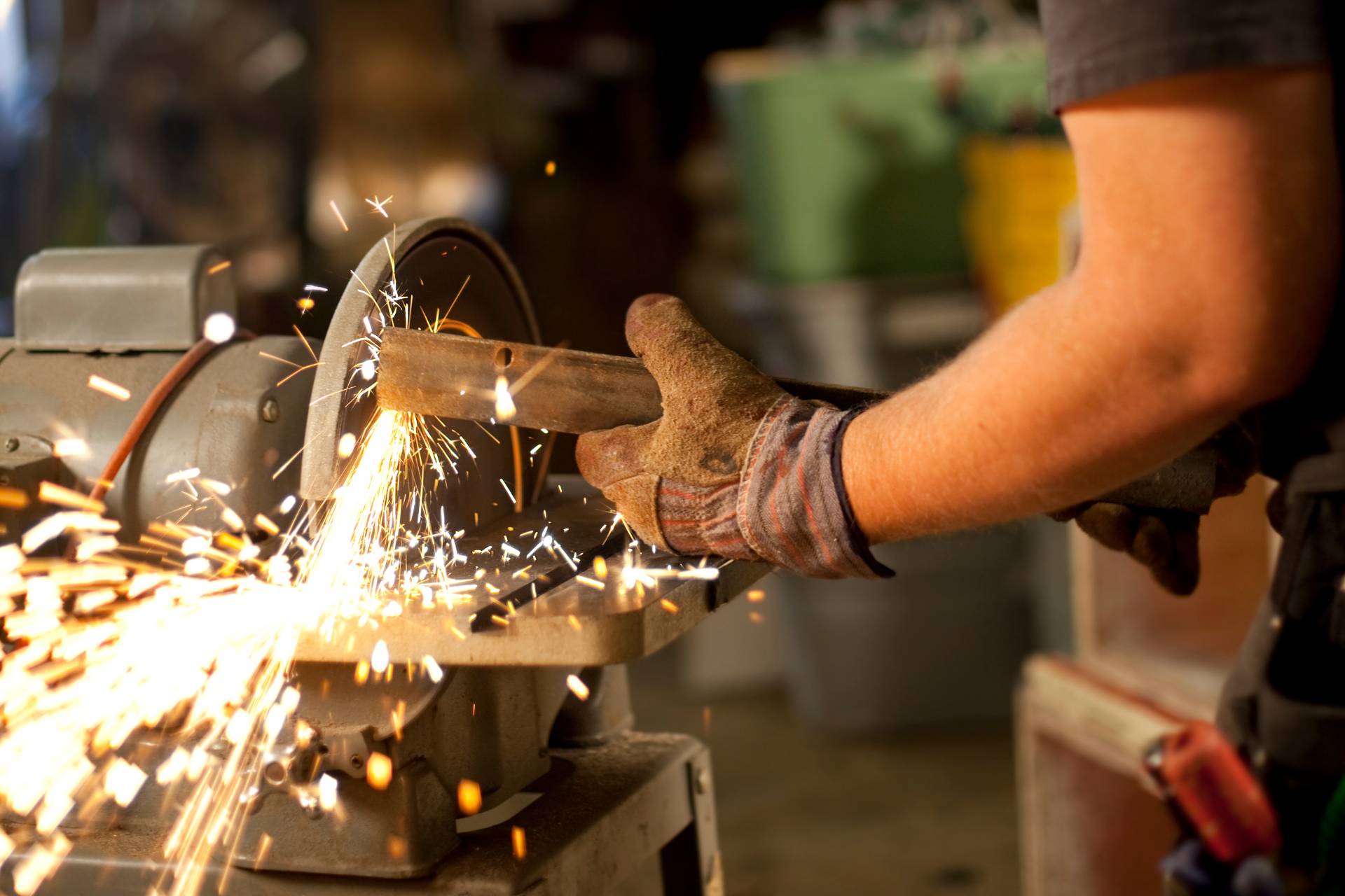 Worker using a stationary disc sander in a workshop with sparks flying, illustrating proper use and safety gear Worker using a stationary disc sander in a workshop with sparks flying, illustrating proper use and safety gear