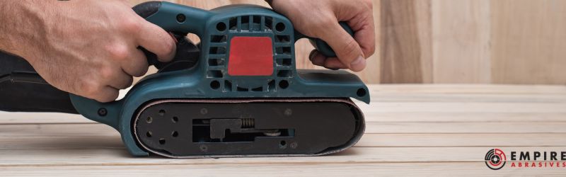 Professional using an electric belt sander on a wooden surface to achieve a fine, smooth finish